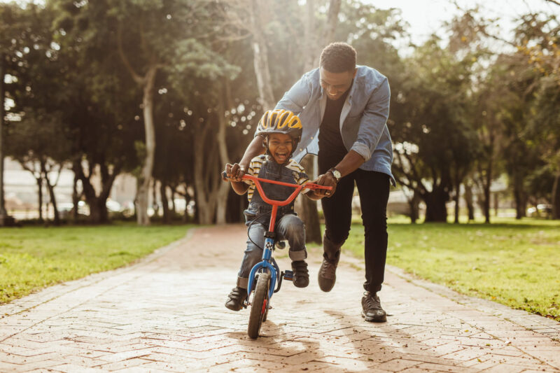 foster parent teaching child to ride a bike and large smiles