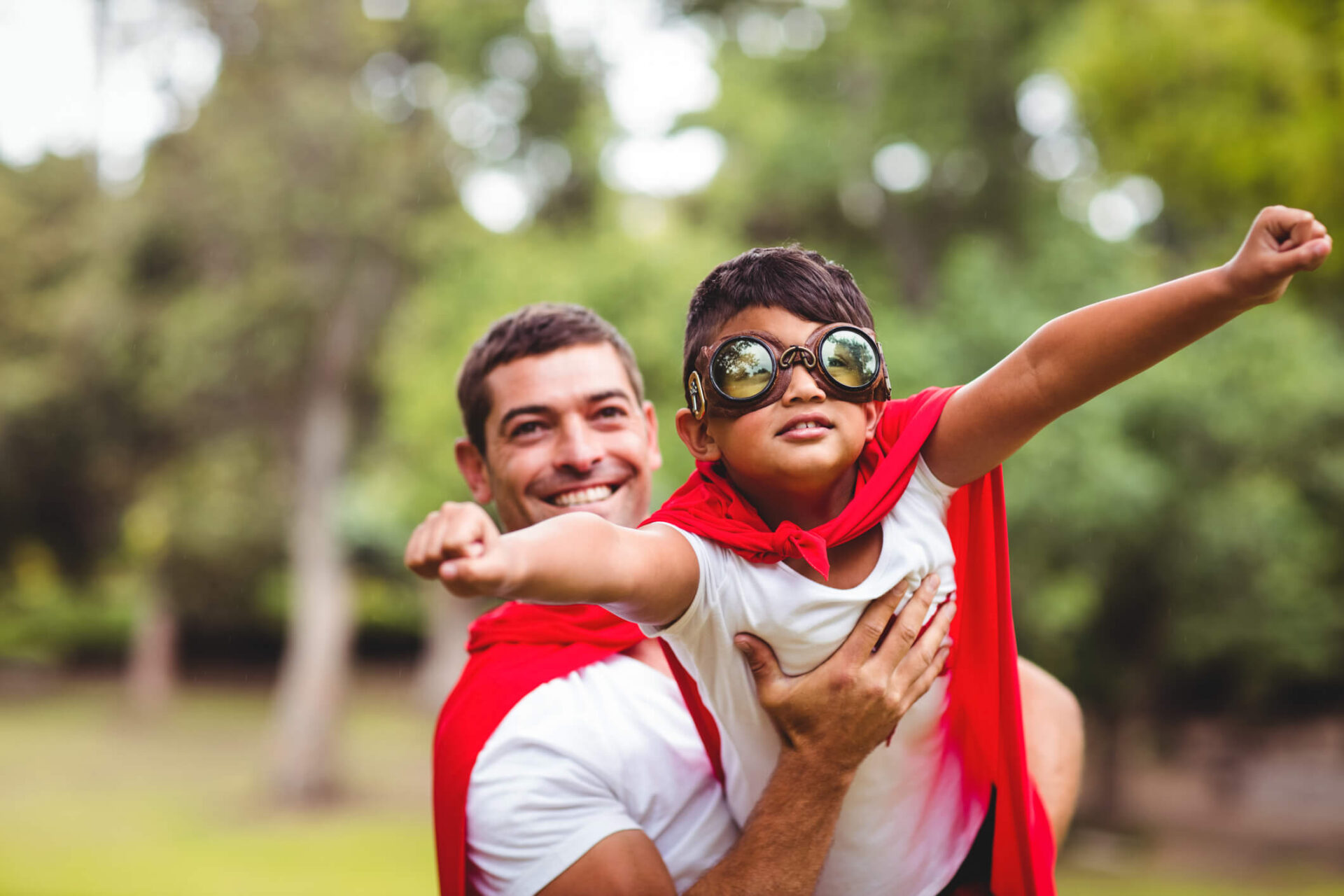 Foster parent and child dressed in superhero costumes while parent holds child pretending to fly.